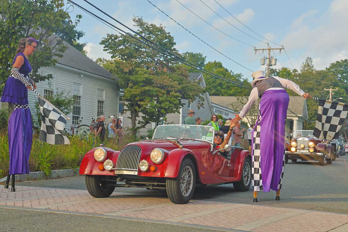A stilt walker high-fives a woman in a historic race car during the parade.