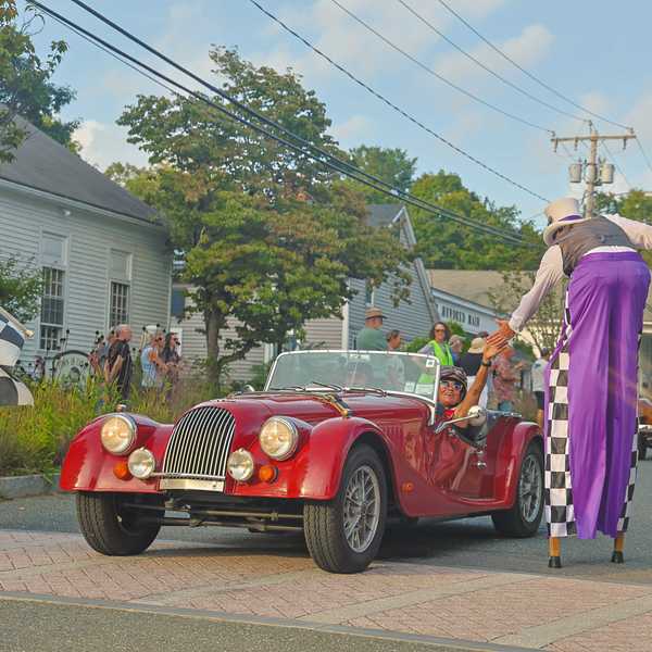 A stilt walker high-fives a woman in a historic race car during the parade.